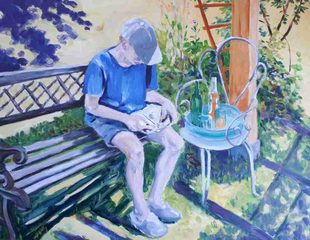 A young boy sitting on a bench in a garden, absorbed in reading a book, with a small table nearby holding a few drinks.