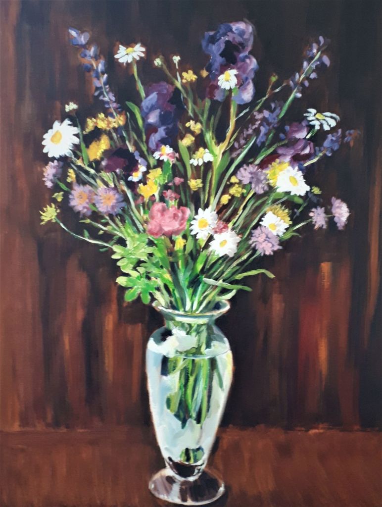 A vibrant floral arrangement in a transparent vase, featuring a mix of colorful flowers like daisies, lavender, and roses, set against a dark wooden background.