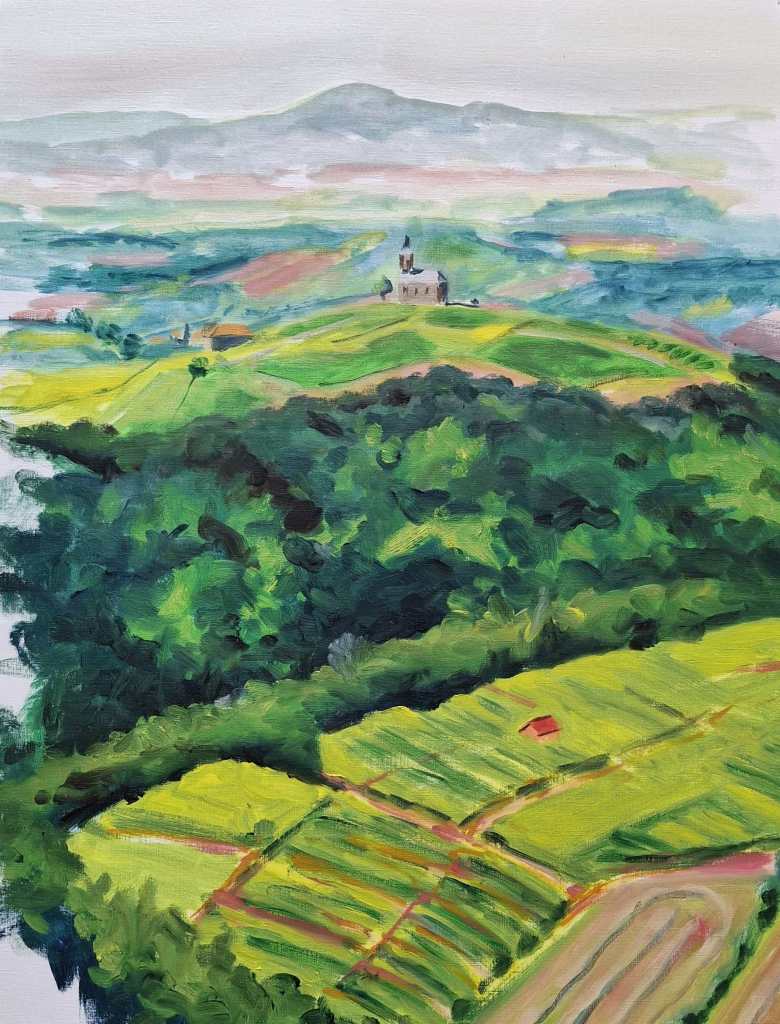 Aerial view of lush green hills with terraced fields and a small church in the distance, surrounded by misty mountains.